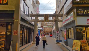 Nishiki Tenmangu Shrine is located at the eastern end of Nishiki-koji Street, where Kyoto's Nishiki Market is located. Its torii gate is pierced by buildings on both sides.